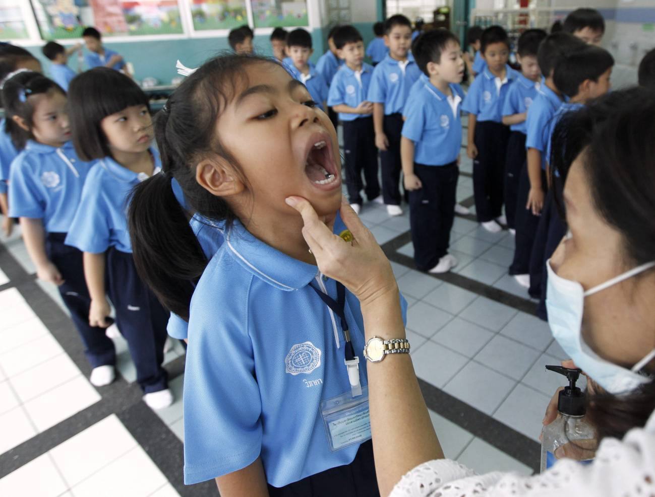 Una profesora tailandesa revisa la boca de un estudiante durante una campaña de control de la fiebre aftosa.