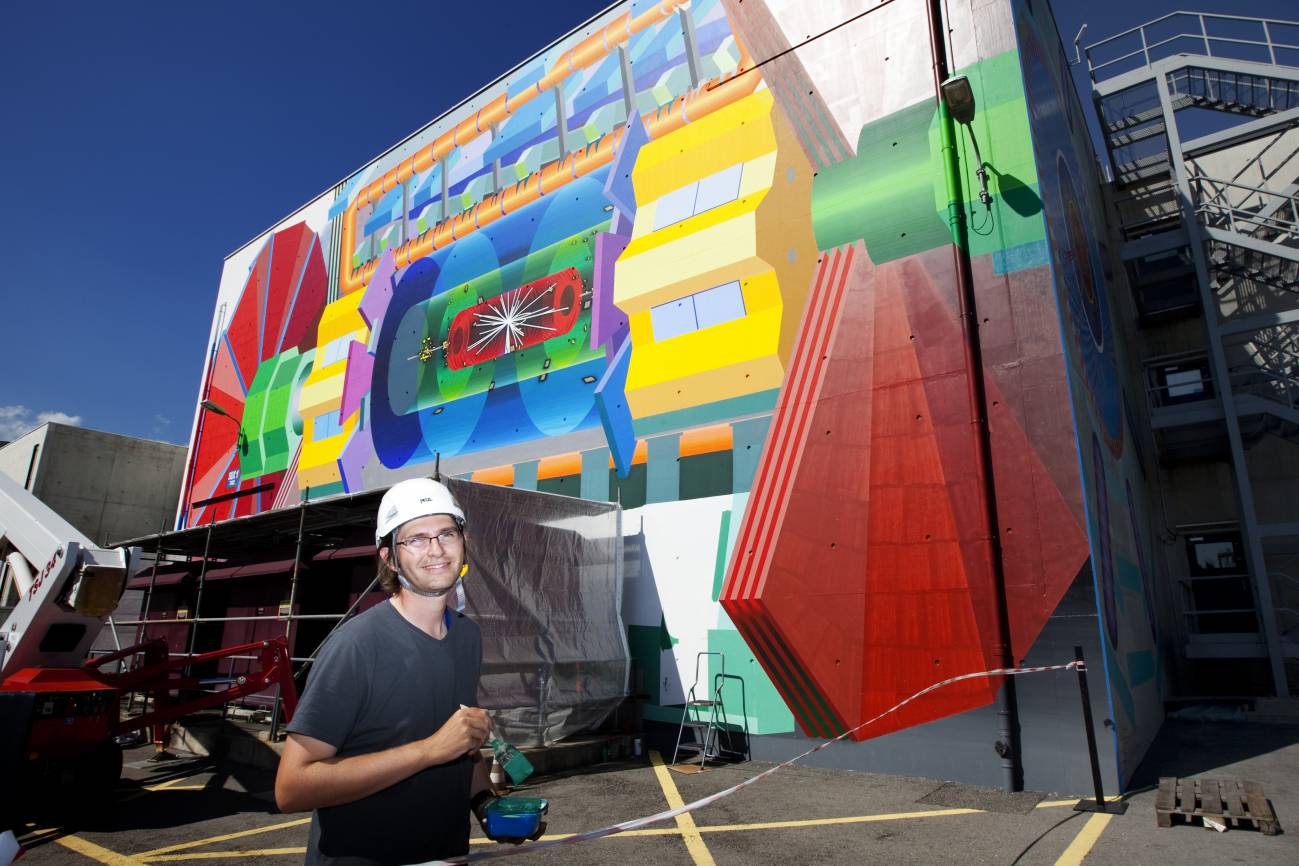 El artista estadounidense Josef Kristofoletti, ante el mural del ATLAS en el CERN