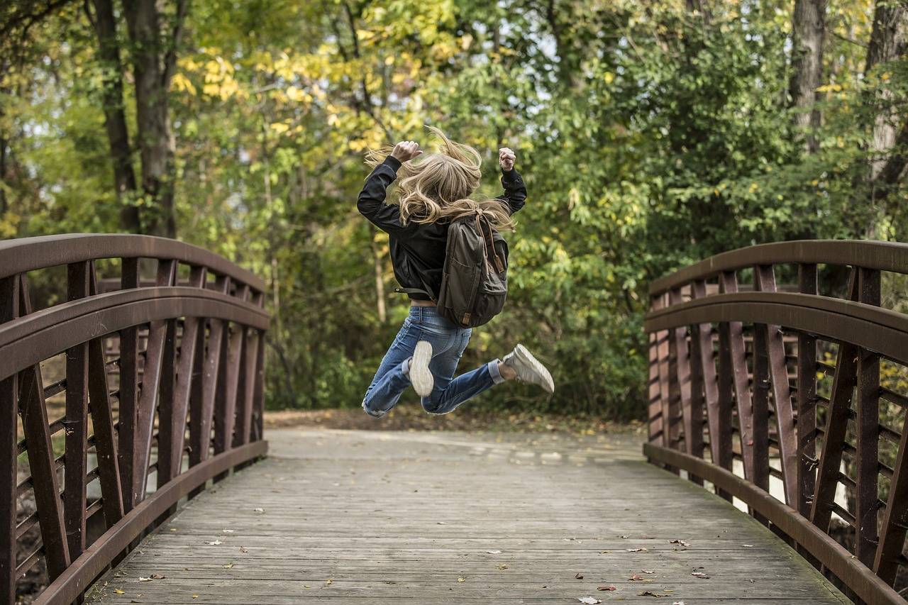 niña con mochila saltando en un puente
