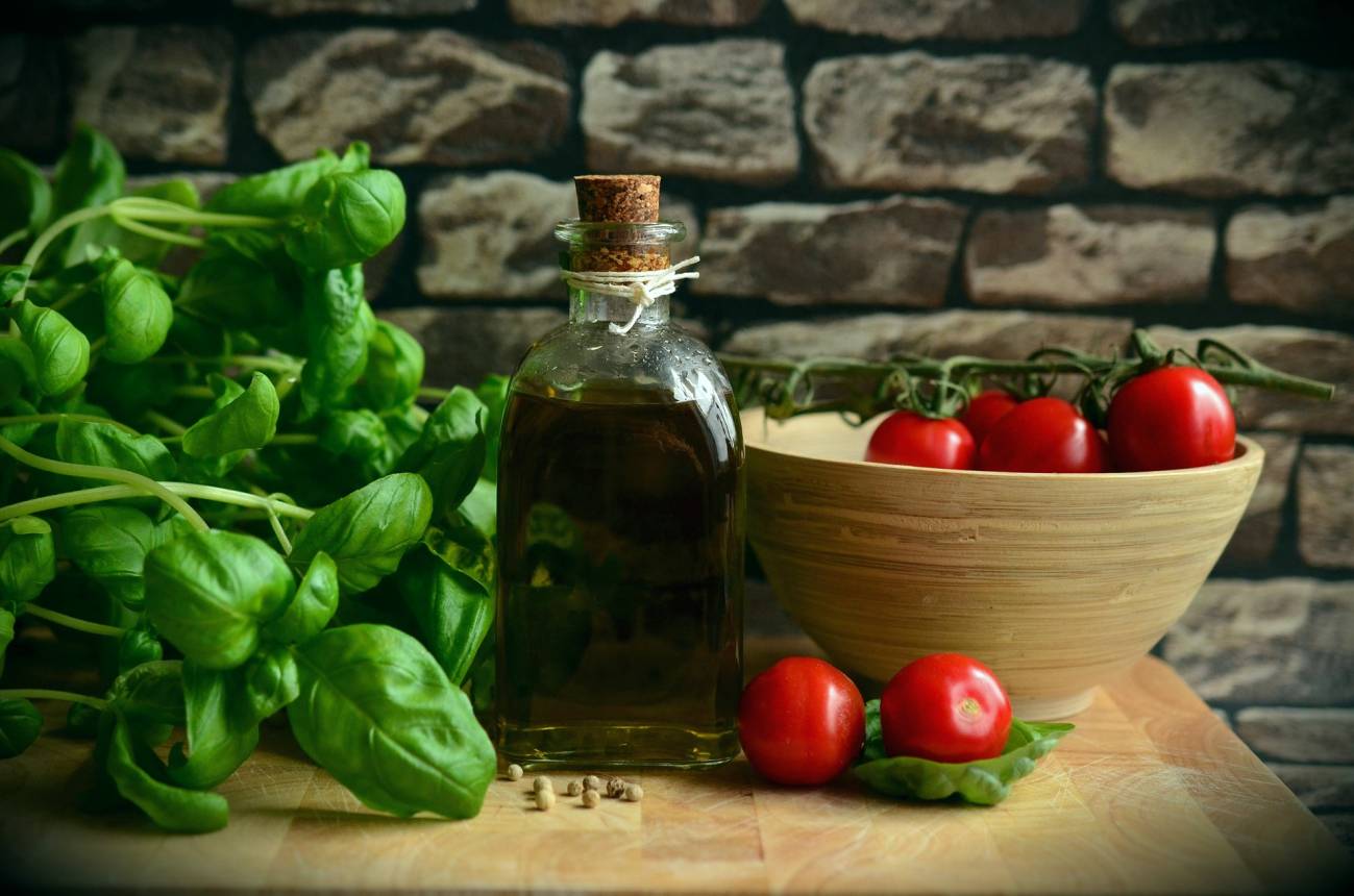 Productos típicos de la dieta mediterránea sobre una mesa de madera: una botella de aceite, un cuenco con tomates y hojas de albahaca