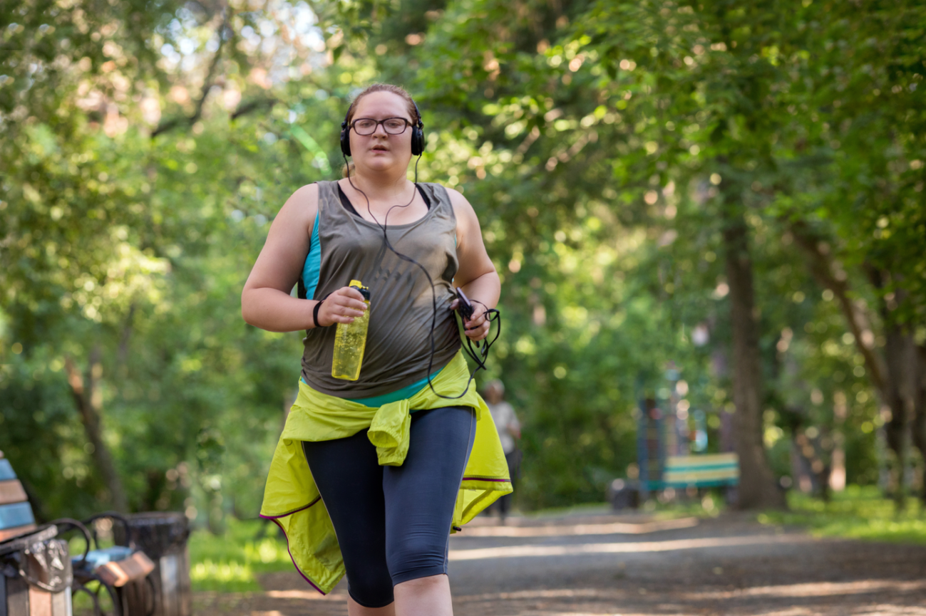 mujer con sobrepeso corriendo por un parque