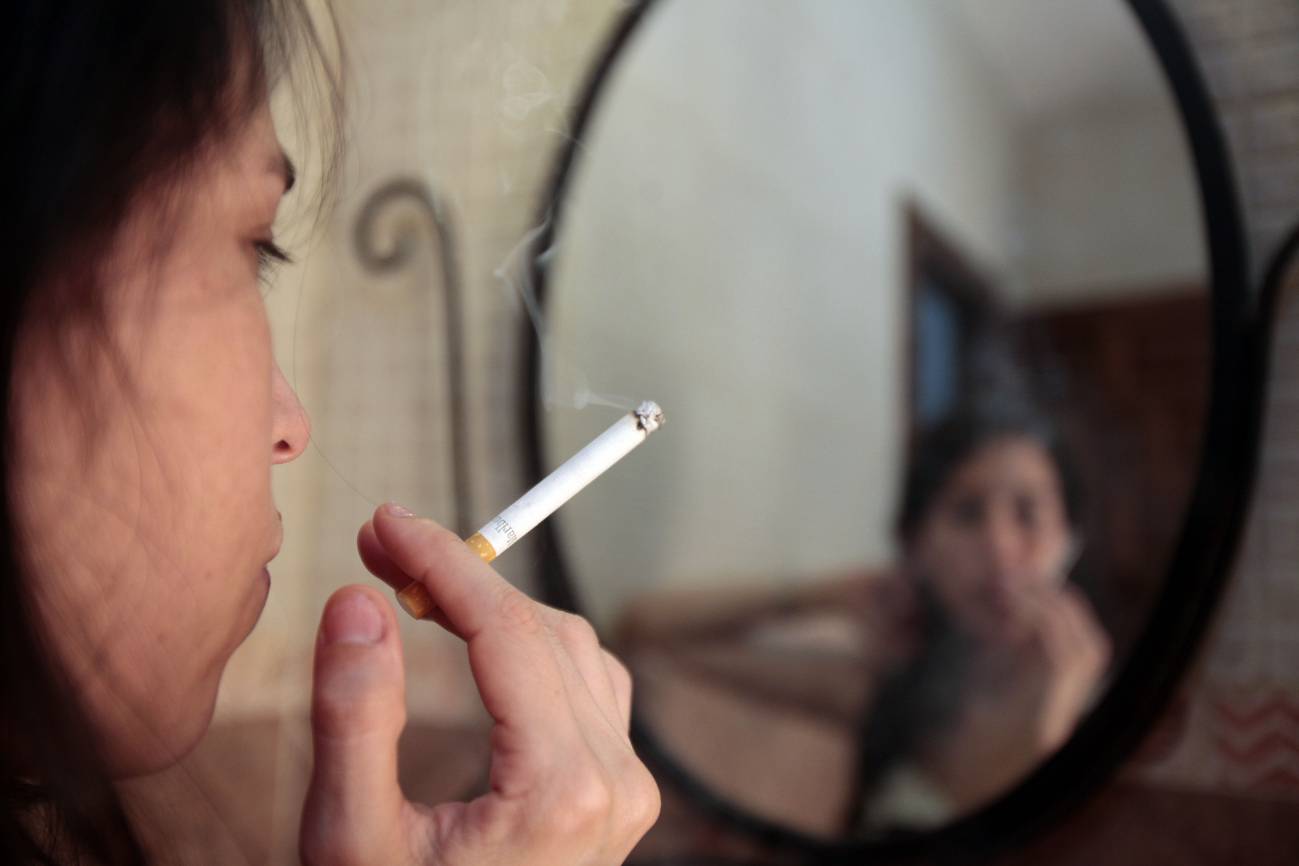 Chica fumando un cigarrillo delante de un espejo