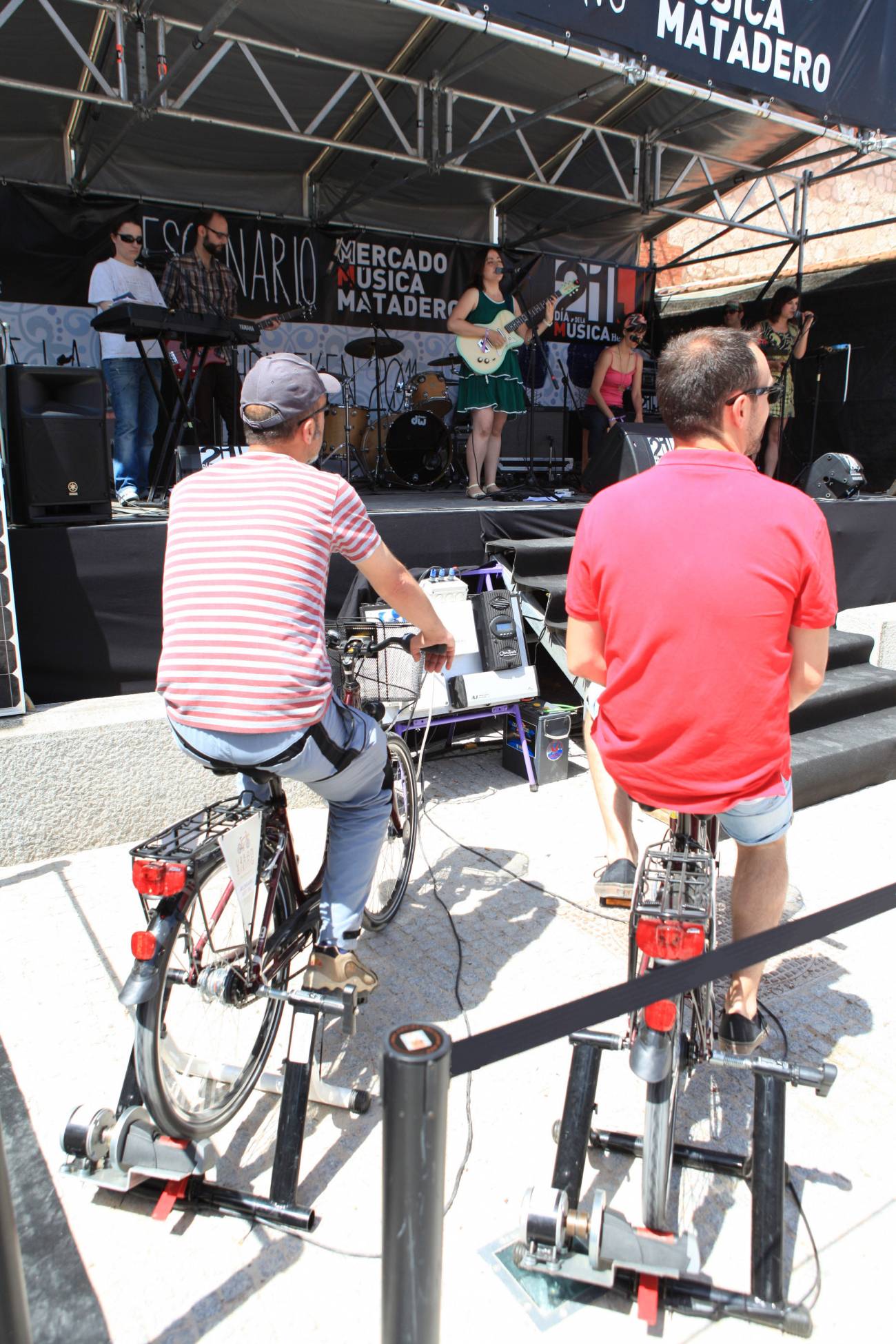 Dos asistentes del festival pedaleando en bici estática delante de un escenario